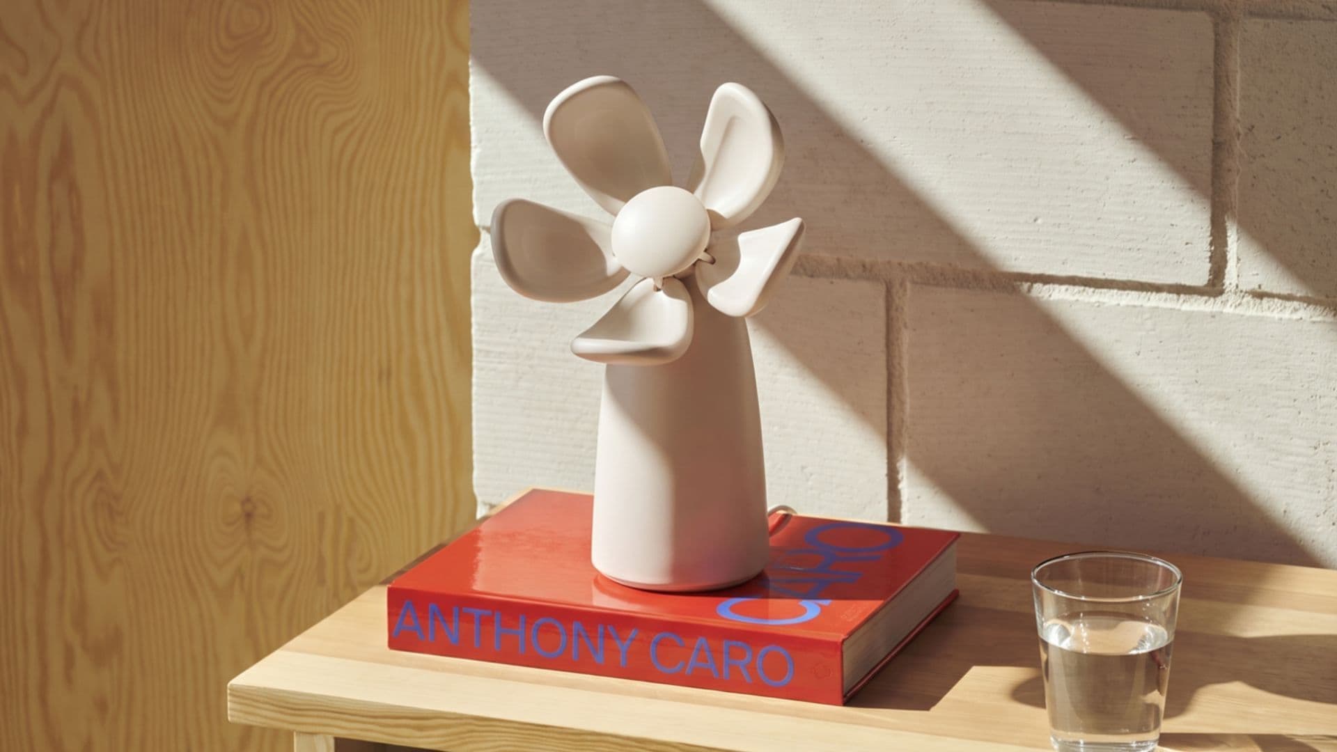 The white flower-shaped Bloomie monitor with open petals, sitting on a book on a wooden side table