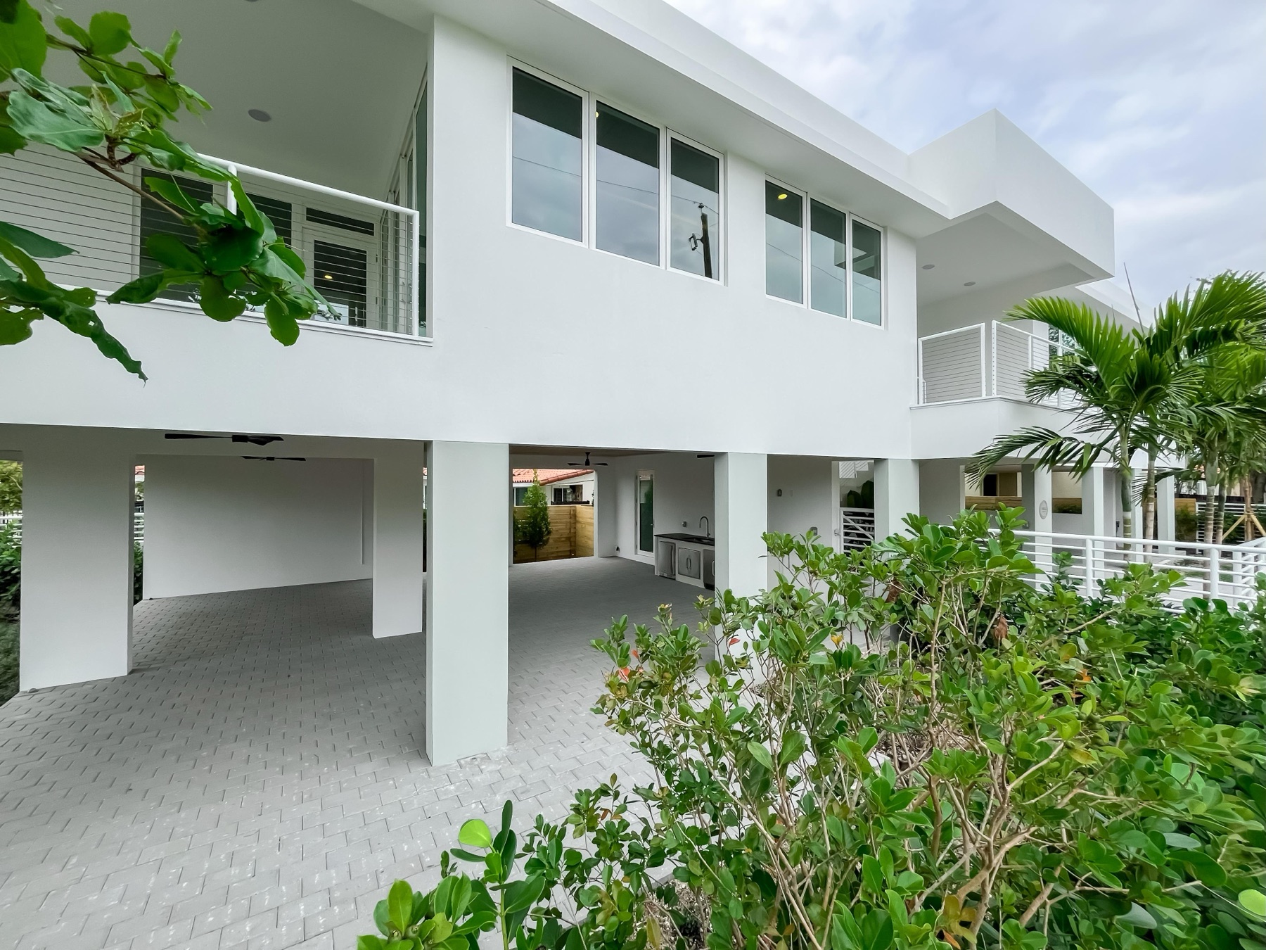 CM1's white living volume elevated on columns above an open ground level with a summer kitchen and paver courtyard