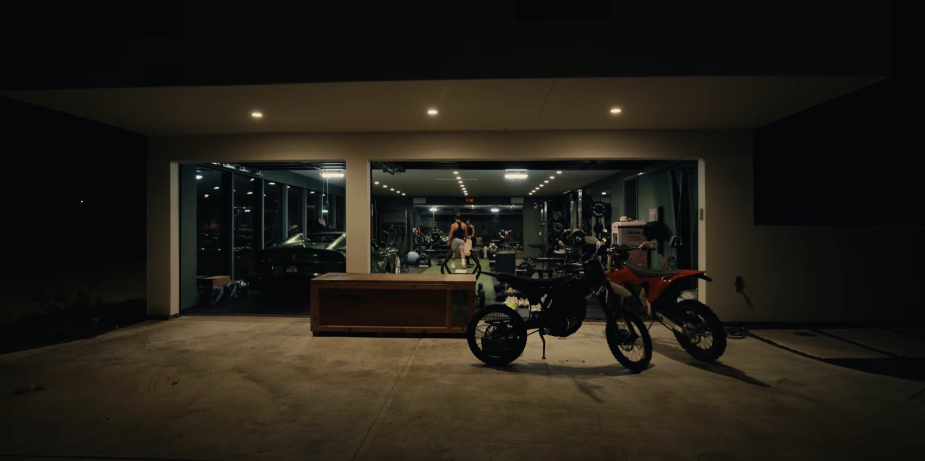 Night exterior of Greg LaVecchia's garage gym with bikes parked outside and the lit gym visible through glass doors