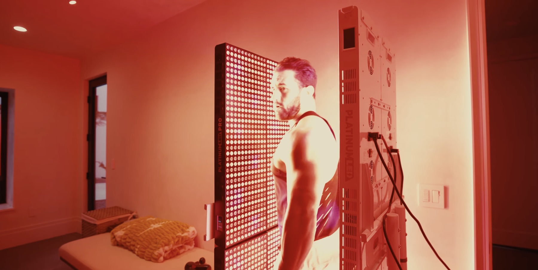 Greg LaVecchia standing beside a bright full-body PlatinumLED red light panel in a warm-lit recovery room
