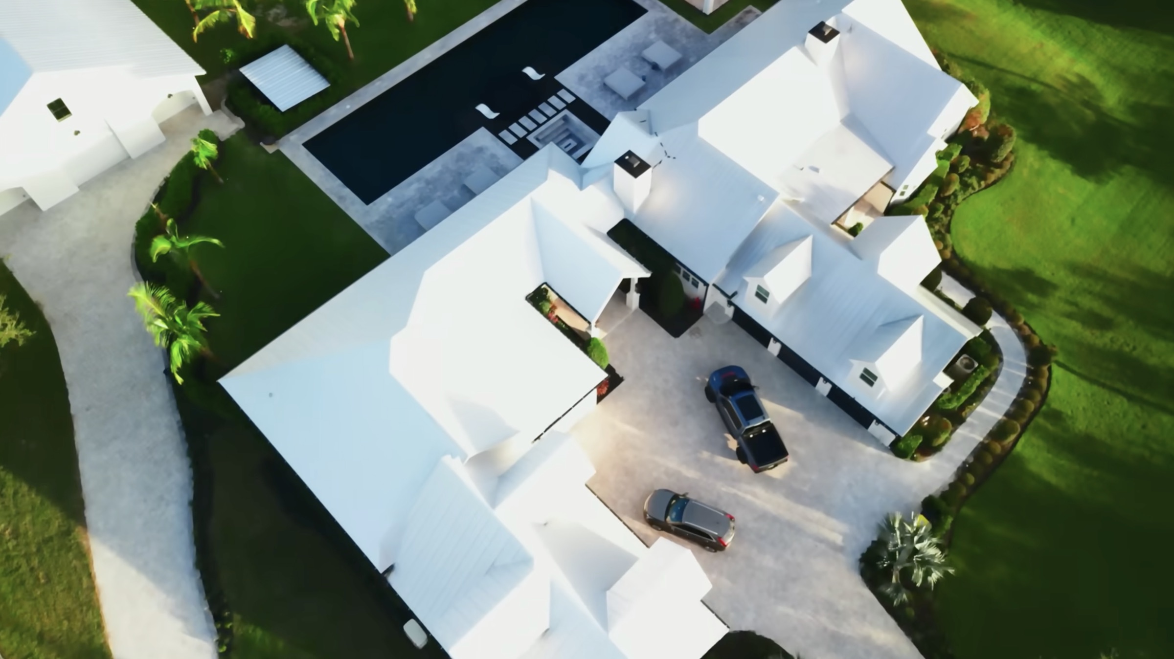 Aerial view of Dom Iacovone's white-roofed Florida estate with the main residence, pool, driveway, and secondary garage building visible from above
