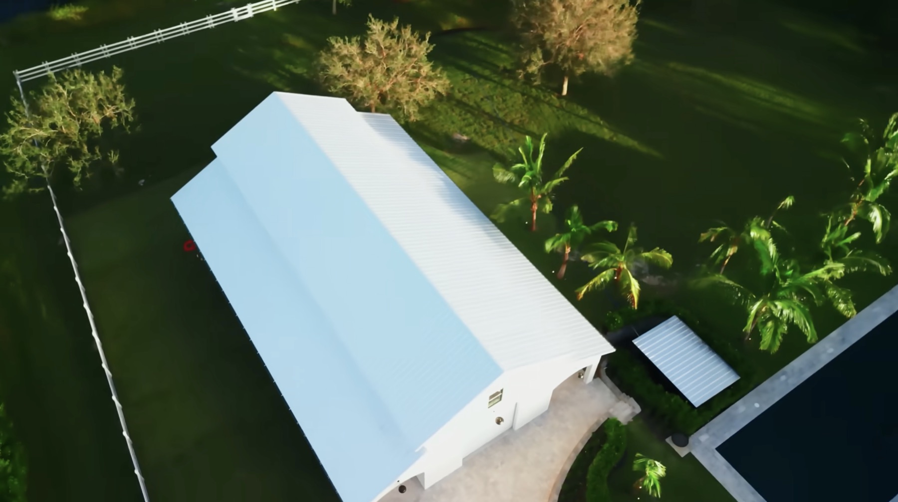 Aerial view of the white secondary garage building beside a pool, palm trees, green lawn, and a matching light-colored driveway