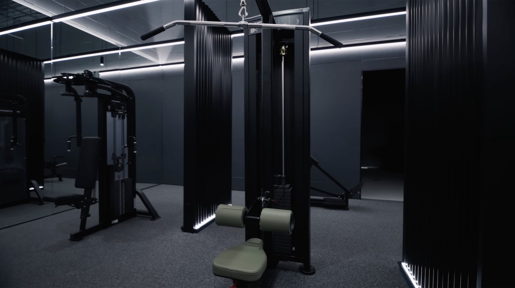 A black lat pulldown machine framed between two tall fluted columns with vertical white LED strips, a functional trainer cable station visible in the background against dark gray walls